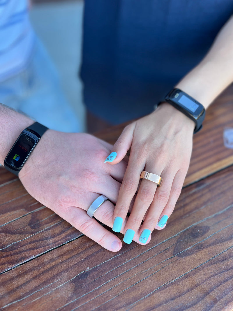 Two hands with rings on a wooden surface, one hand wearing a smartwatch.
