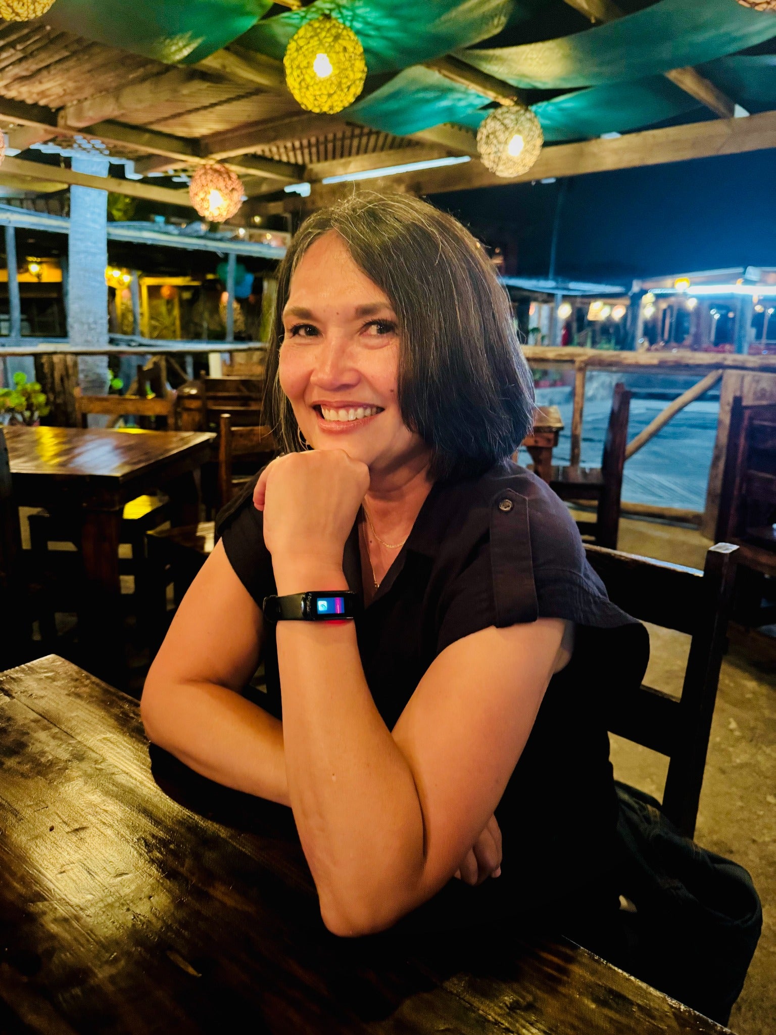 A smiling woman wearing a wrist wearable in a warmly lit evening setting